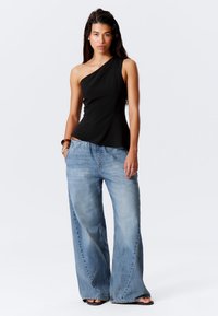 Schwarzes Top mit einem Schulterträger, kombiniert mit hellblauen weit geschnittenen Jeans. Der Stoff ist glatt und die Jeans haben eine leichte Verwaschung sowie eine lockere Passform.