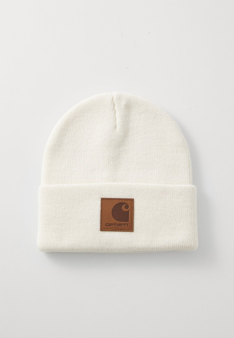 Gorro de punto blanco con puño doblado. Presenta un parche de cuero marrón con el logo de Carhartt. Textura suave y forma redondeada.