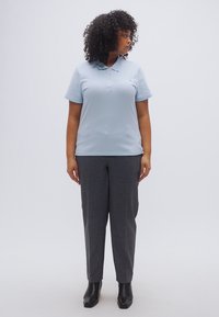 Ανοιχτό μπλε πόλο πουκάμισο με γιακά, συνδυασμένο με γκρι καρό παντελόνι. Το μοντέλο φοράει μαύρα μποτάκια αστραγάλου, με τα μαλλιά σε χαλαρές μπούκλες.