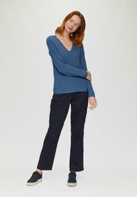 Blau gestreifter, langärmeliger V-Ausschnitt-Pullover, kombiniert mit schwarzen Cargo-Hosen mit Seitentaschen und schwarzen Sneakers mit strukturierten Sohlen.
