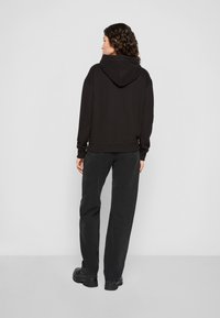 Μαύρος κοντός φούτερ με κουκούλα, μαλακή υφή και ραμμένα μανίκια, συνδυασμένος με φαρδιά μαύρα τζιν και χοντρά μαύρα μποτάκια.