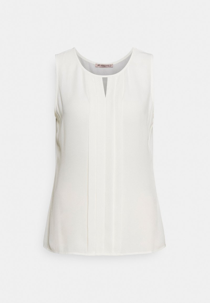 Blouse blanche sans manches avec un col rond, des plis verticaux centraux et une petite encoche en forme de V au col avant.