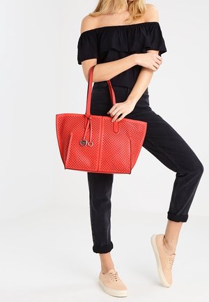 Red perforated tote bag with two handles, featuring a spacious interior and round hardware accents, set against a light background.