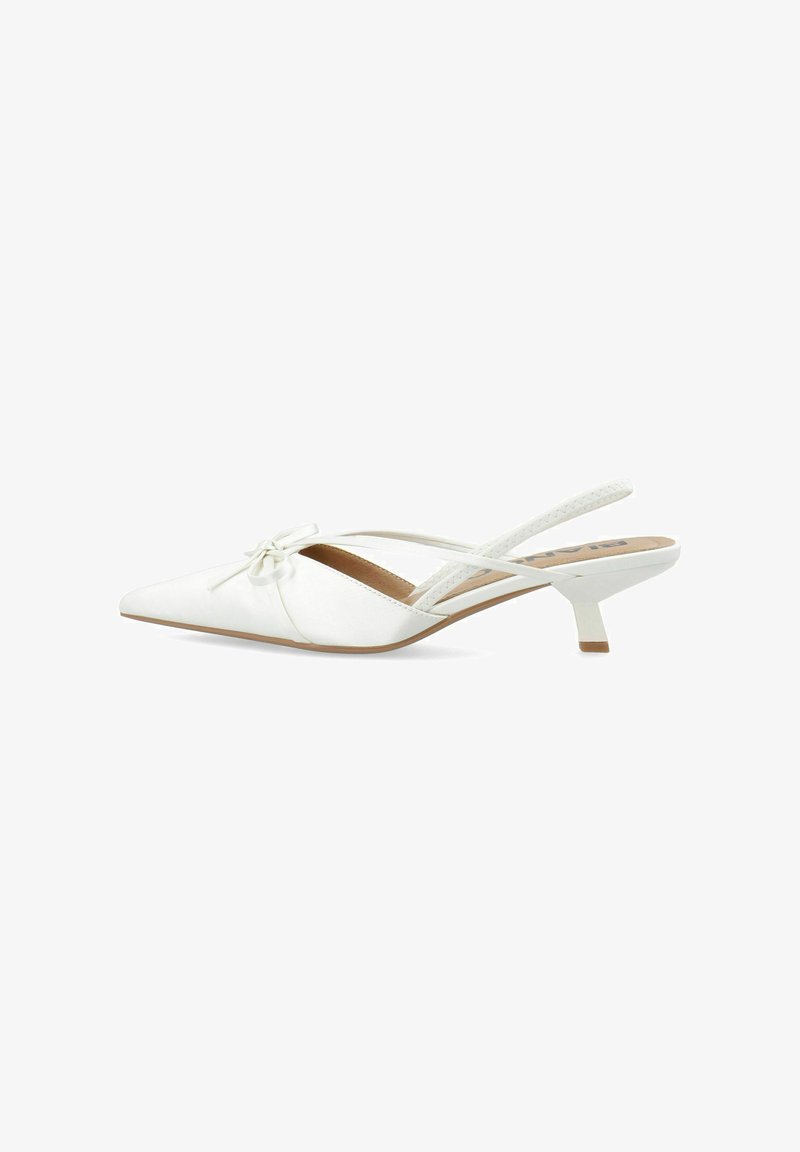 Zapato blanco de tacón bajo tipo kitten heel con punta puntiaguda, tiras delgadas y un pequeño lazo decorativo en la parte frontal, presentado sobre un fondo blanco liso.