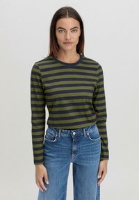 Langärmeliges gestreiftes Hemd in olivgrün und dunkelgrau, mit Rundhalsausschnitt, kombiniert mit hochgeschnittenen blauen Jeans.