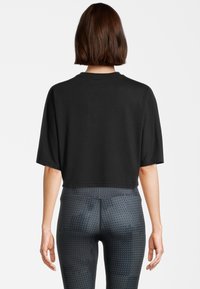 Felpa nera corta con maniche corte, realizzata in materiale morbido. Abbinata a leggings aderenti e stampati in tonalità scure.