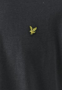 T-shirt nera in cotone con un piccolo logo di un'aquila ricamato in giallo sul petto. Il tessuto è morbido e ha una vestibilità classica.