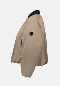 Giubbotto bomber beige con colletto a coste nero, tasca frontale e una patch circolare nera sulla manica sinistra. Tessuto liscio e leggermente lucido.