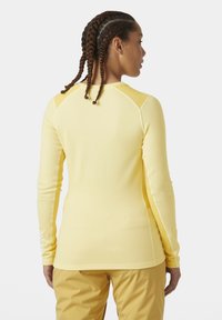 Dlouhý rukáv, přiléhavý top vyrobený z měkké, lehké látky v pastelově žluté barvě. Obsahuje raglánové rukávy a ploché švy pro pohodlí.