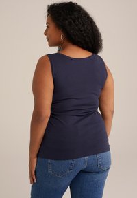 Top sin mangas de color azul marino hecho de tela suave, con escote redondo y un diseño ajustado, combinado con jeans de mezclilla de color azul claro.