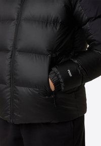 Svart boblejakke med zip-lukking, quiltet design og elastiske mansjetter. Har en liten logo på ermet og en lomme ved livet.