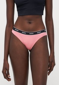 Rosa bomullsstringtruse med en svart elastisk midjebånd som har "HUGO" logo. Glatt tekstur og tettsittende design.