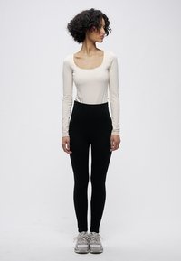 Hosszú ujjú, krémszínű felső mély kivágással, magas derekú fekete leggingsszel párosítva. A ruházat sima textúrájú és elegáns kialakítású.