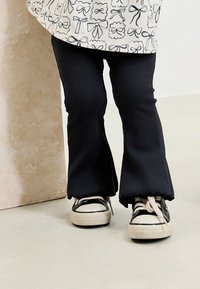 Black ribbed flared pants with raw edges paired with black and white low-top sneakers featuring white soles and beige laces.
