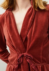 Vestido envolvente de terciopelo rojo con escote en V profundo, detalle de hombro fruncido y cinturón atado en la cintura. Textura suave y acabado liso.