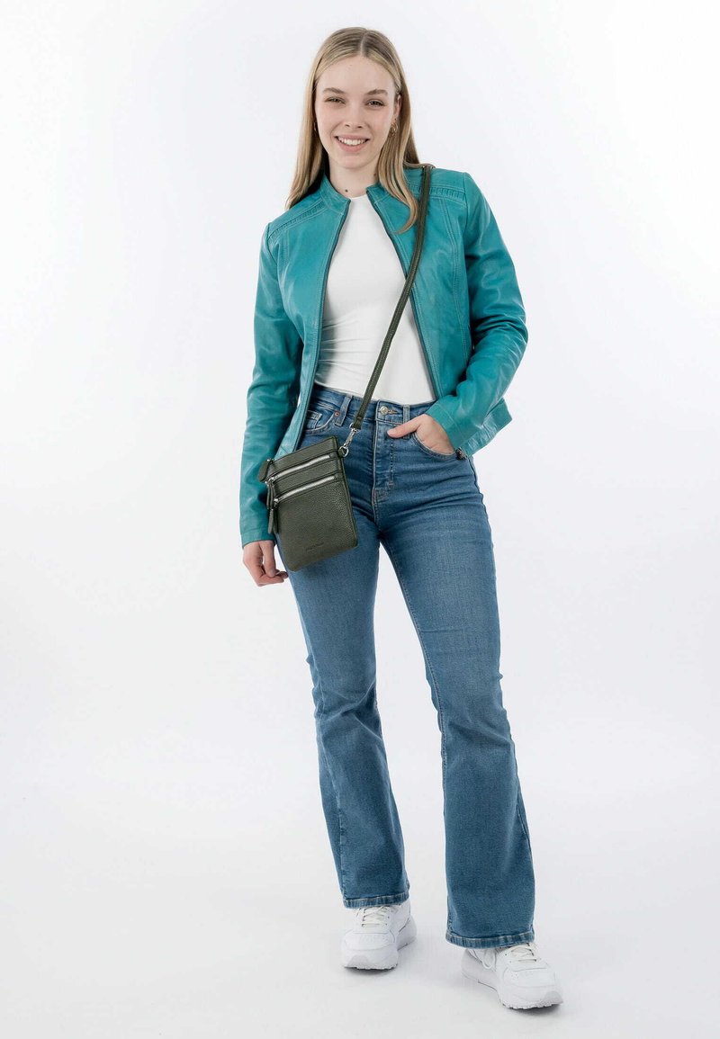 Teal leather jacket with a zip closure, white top, and blue flared jeans. Holding a small green crossbody bag with zipper accents.