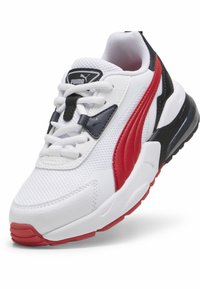 Sneaker atletico bianco in materiali mesh e pelle, con accenti rossi e neri, punta arrotondata e suola testurizzata per una migliore aderenza.