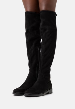 Botas negras de ante por encima de la rodilla, con cremallera lateral, suela plana y textura suave. Con un borde superior doblado como acento.
