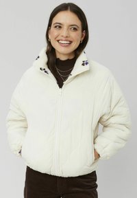 Veste en crème matelassée avec un col en fourrure, broderie florale violette sur le col, et poignets élastiques, dotée d'une fermeture éclair à l'avant et de poches latérales.