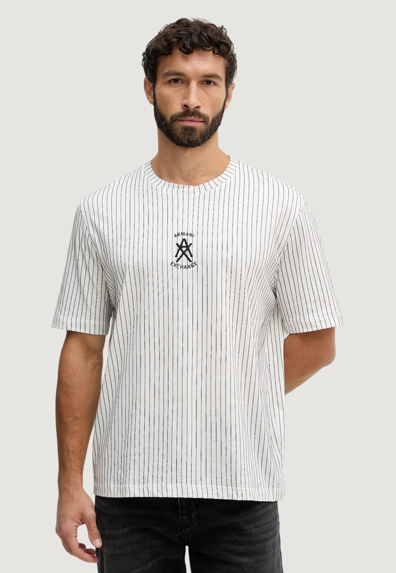 T-shirt blanc à manches courtes avec des rayures noires verticales, un col rond et un logo noir centré sur la poitrine.
