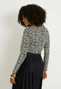 Top de manga larga con estampado de leopardo en blanco y negro, combinado con una falda negra plisada. El conjunto cuenta con una cintura ajustada.