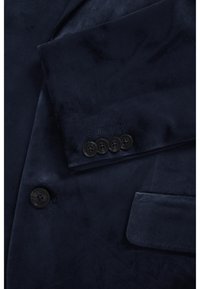 Marineblauer Samtblazer mit abgestepptem Revers, einer Brusttasche und vier schwarzen Knöpfen am Ärmelabschluss. Glatte Textur mit dezentem Glanz.