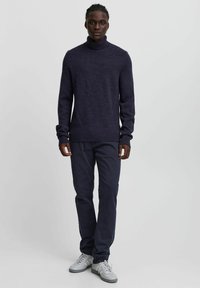 Navy blue turtleneck sweater in textured knit paired with dark trousers. Worn with light gray sneakers. Simple and fitted design.