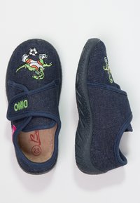 Marine blauwe stofpantoffels met een rubberen zool. Voorzien van een groene geborduurde hagedis die voetbalt. Klittenbandsluiting voor eenvoudig aantrekken.