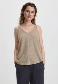 Top senza maniche beige a scollo a V in tessuto leggero, con una vestibilità comoda e una texture sottile. Abbinato a pantaloni scuri.