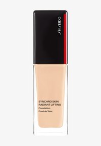 Foundationfles met een zwarte dop en rode accenten, heldere glazen body, met een pale beige vloeistof, gelabeld "Synchro Skin Radiant Lifting."