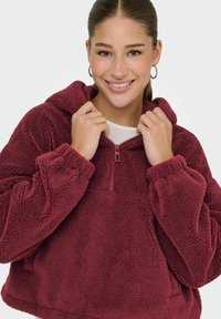 Burgundijski flis pulover s kapuljačom, s polu-zip prednjim dijelom, teksturiranom površinom i elastičnim manžetama za udobno prianjanje.
