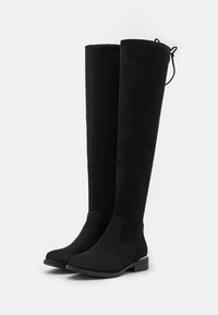 Bottes noires au-dessus du genou en suède doux avec une fermeture éclair latérale, un bout arrondi et un petit accent doré sur le talon.
