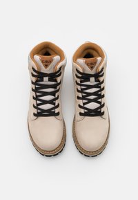 Bottes de randonnée beiges avec une tige en daim, des accents en cuir marron, six œillets noirs, des lacets noirs et une semelle extérieure noire robuste.