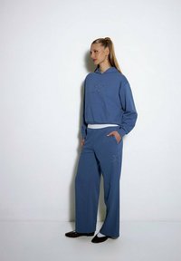 Niebieska bluza z kapturem i pasujące spodnie z designem gwiazdy w diamencikach. Materiał wydaje się miękki, z luźnym krojem i bocznymi kieszeniami.