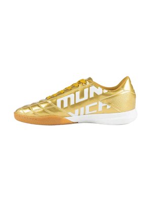 Zapatilla de fútbol sala dorada con cordones amarillos, suela blanca y gran texto blanco "MUNICH" en el lateral.