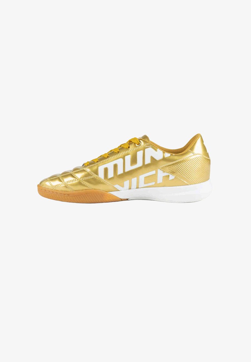 Chaussure de football d'intérieur dorée avec lacets jaunes, semelle blanche et grand texte blanc "MUNICH" sur le côté.