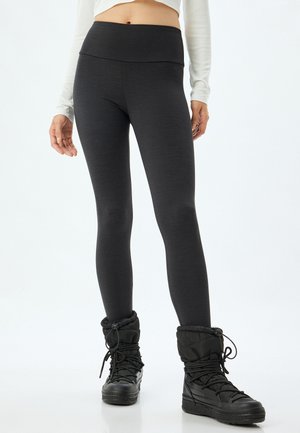 Schwarze Leggings mit hohem Bund, aus strukturiertem Stoff. Kombiniert mit schwarzen, isolierten Stiefeln mit gepolstertem Kragen und Schnürsenkeln.