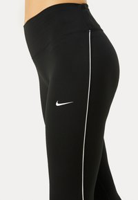 Črne športne legice imajo visok pas, bele stranske črte in belo Nike logo na levem stegnu. Izdelane so iz raztegljivega materiala.