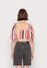 Top corto a righe con maniche a sbuffo, caratterizzato da tonalità arancioni, rosa e nere. Abbinato a pantaloni corti in denim scuro a vita alta.