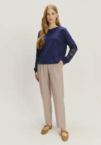 Granatowy sweter z koronkowymi detalami na rękawach, zestawiony z jasnobeżowymi, dopasowanymi spodniami i brązowymi balerinami. Gładki materiał z luźnym krojem.