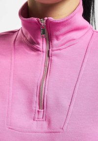 Felpa zip-up rosa con colletto alto, tessuto testurizzato e cuciture decorative nella zona del petto, dotata di zip in metallo.