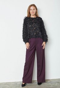 Juodas permatomas viršus su tekstūruotu gėlių raštu, ilgomis rankovėmis, derinamas su aukštu liemeniu, plačiomis violetinėmis kelnėmis ir juodomis aukštakulnėmis bateliais.