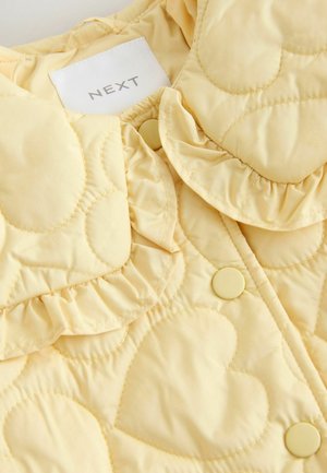 Gul quiltet jakke med hjerteformede mønstre, rynket krave og matchende knapper. Mærket med "NEXT" tag indeni.