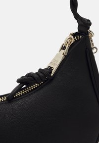 Sac à main en cuir noir texturé avec fermeture éclair dorée et tirette de fermeture éclair en métal de marque, avec un détail de sangle en cuir nouée.