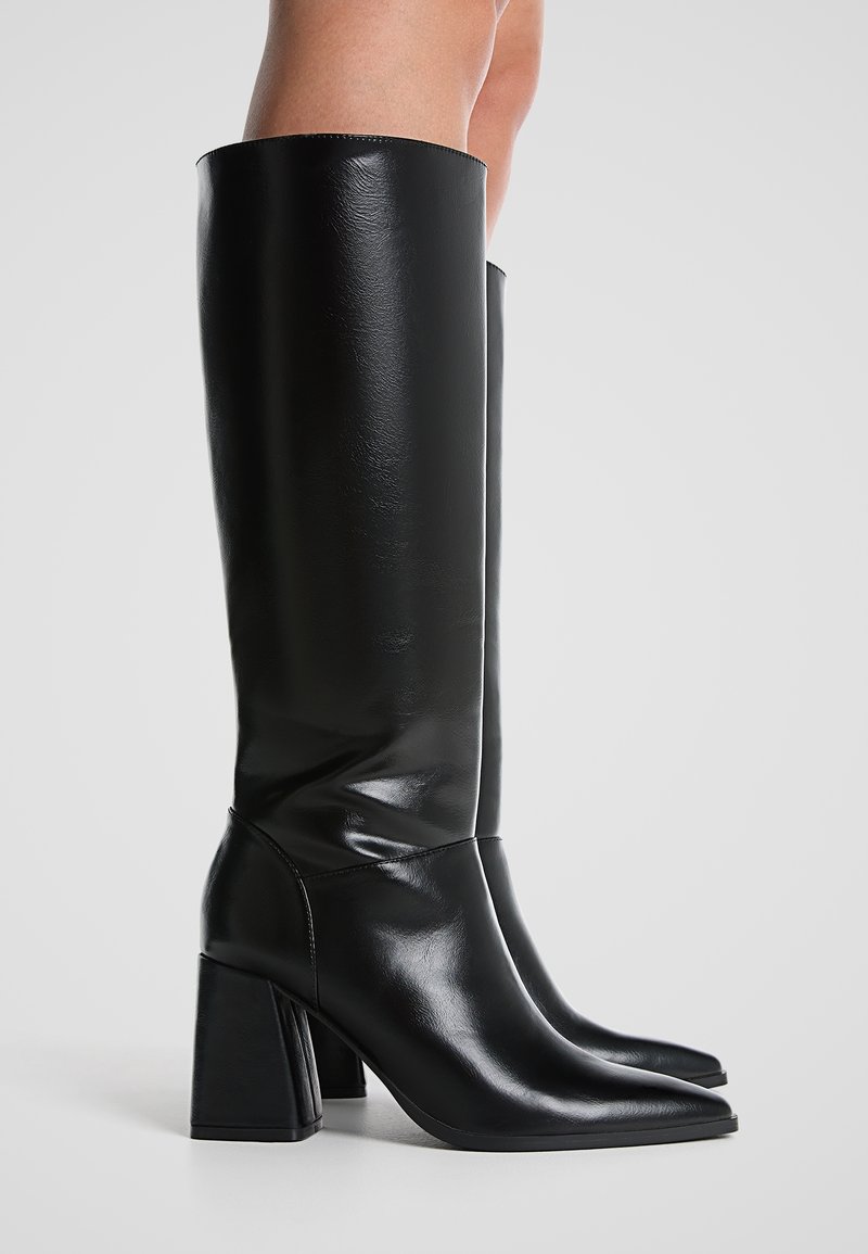 Bottes noires montantes en cuir lisse avec une pointe effilée et un talon carré épais. Présente un design épuré et une finition brillante.
