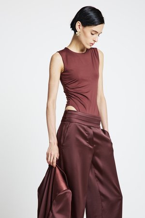 Burgundy sleeveless top with side ruching, paired with wide-leg trousers in matching satin. The outfit features a sleek silhouette with minimalistic design.