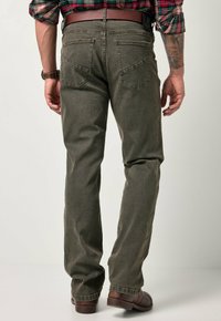 Jeans in denim verde oliva con un design a gamba dritta, dotati di due tasche posteriori e una leggera texture. Indossati con scarpe in pelle marroni.