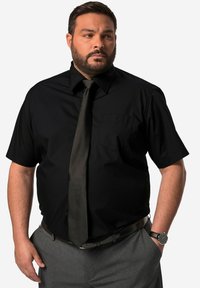 Zwart T-shirt met korte mouwen en een zak, gecombineerd met een donkere stropdas en grijze broek. Heeft een gestructureerde riem en een zwart polshorloge.