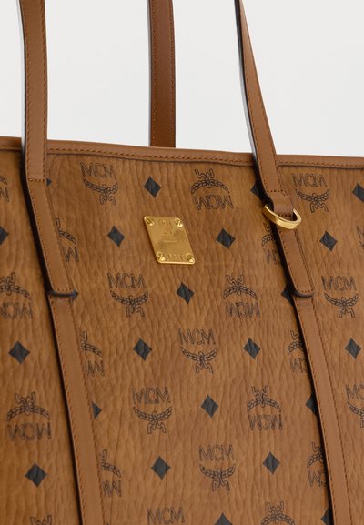 Sac cabas en cuir marron texturé avec motif noir du logo MCM et plaque de marque en métal doré au centre, avec deux bretelles.