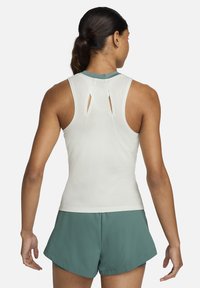 Lichtgekleurde mouwloze top met uitsneden aan de achterkant, gecombineerd met donkergroene shorts, gemaakt van ademend materiaal.